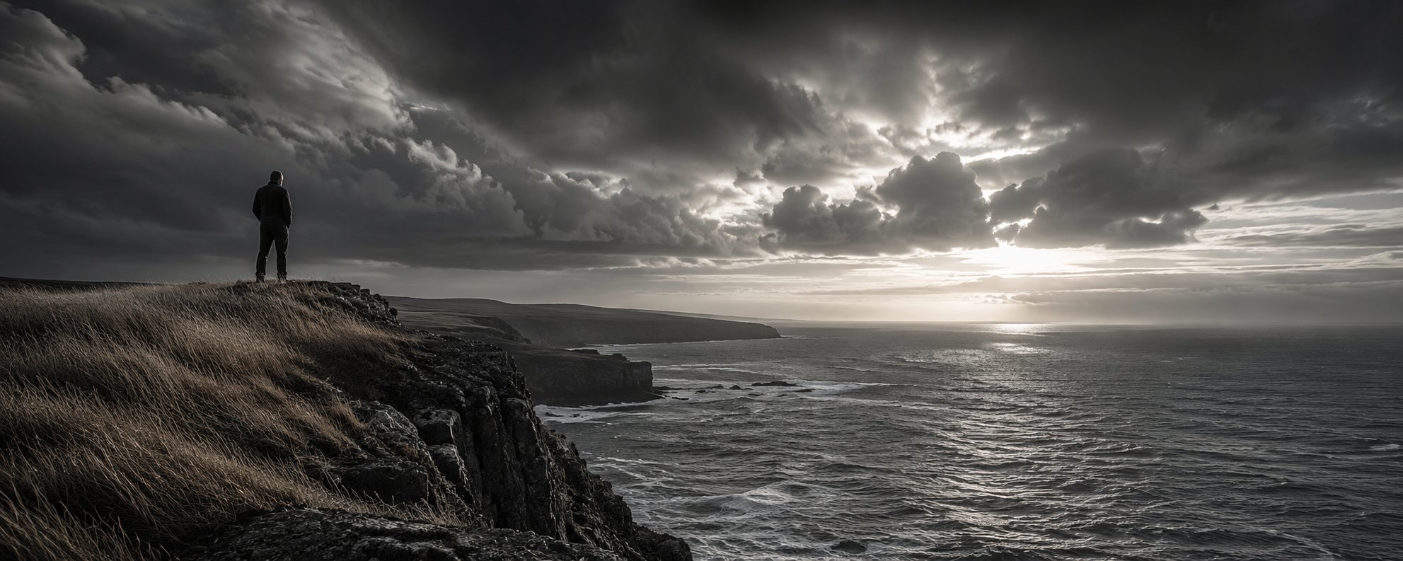 A solitary figure stands at the edge of a cliff overlooking the open ocean at dusk, a single shaft of light breaking through the clouds.